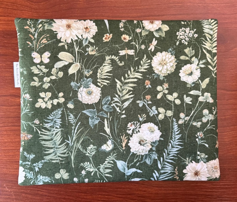 Pu&ograve; includere: Un tessuto rettangolare con un motivo floreale verde con fiori bianchi, farfalle e felci. Il tessuto ha uno sfondo verde scuro con un fitto motivo di elementi botanici. Una piccola etichetta bianca con testo &egrave; visibile sul lato sinistro.