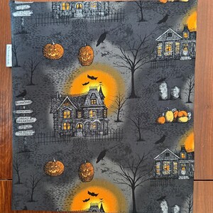 May include: A rectangular fabric panel featuring a Halloween-themed print on a dark gray background. The pattern includes haunted houses, glowing orange moons, jack-o'-lanterns, bare trees, black crows, bats, and signposts with text like Boneyard.