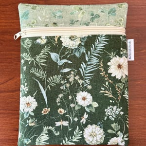Pu&ograve; includere: Una pochette rettangolare con cerniera e design floreale. La pochette presenta uno sfondo verde scuro con fiori bianchi, farfalle ed elementi botanici. La sezione superiore &egrave; verde chiaro con un motivo floreale simile. La cerniera &egrave; beige.