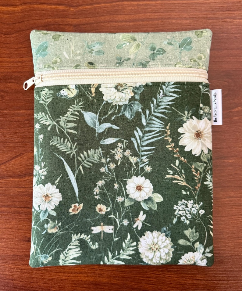 Pu&ograve; includere: Una pochette rettangolare con cerniera e design floreale. La pochette presenta uno sfondo verde scuro con fiori bianchi, farfalle ed elementi botanici. La sezione superiore &egrave; verde chiaro con un motivo floreale simile. La cerniera &egrave; beige.