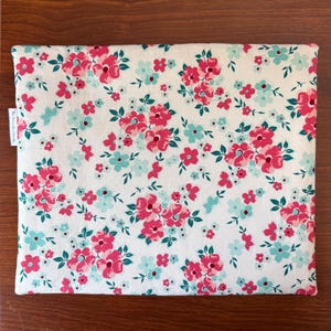 Puede incluir: Una funda rectangular con estampado floral. Presenta un fondo blanco con un patr&oacute;n repetido de flores rosas y turquesas y hojas verdes. La funda tiene un aspecto suave de tela y una peque&ntilde;a etiqueta blanca en el lateral.
