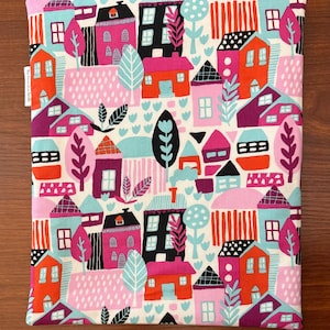 Puede incluir: Una bolsa de tela rectangular con un patr&oacute;n repetitivo y colorido de casas, &aacute;rboles y formas abstractas en tonos rosa, naranja, azul claro, morado, negro y blanco. Una peque&ntilde;a etiqueta de tela blanca con texto negro est&aacute; unida al lado izquierdo.
