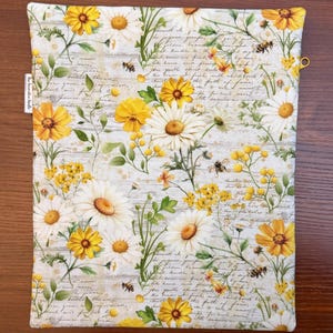 K&ouml;nnte beinhalten: Ein rechteckiger Stoffbeutel mit einem botanischen Druck aus wei&szlig;en und gelben G&auml;nsebl&uuml;mchen, gelben Wildblumen und kleinen Bienen vor einem Hintergrund aus blassem, kursivem Text. Ein kleines wei&szlig;es Stoffetikett mit der Aufschrift The Decoration Needle ist angebracht.