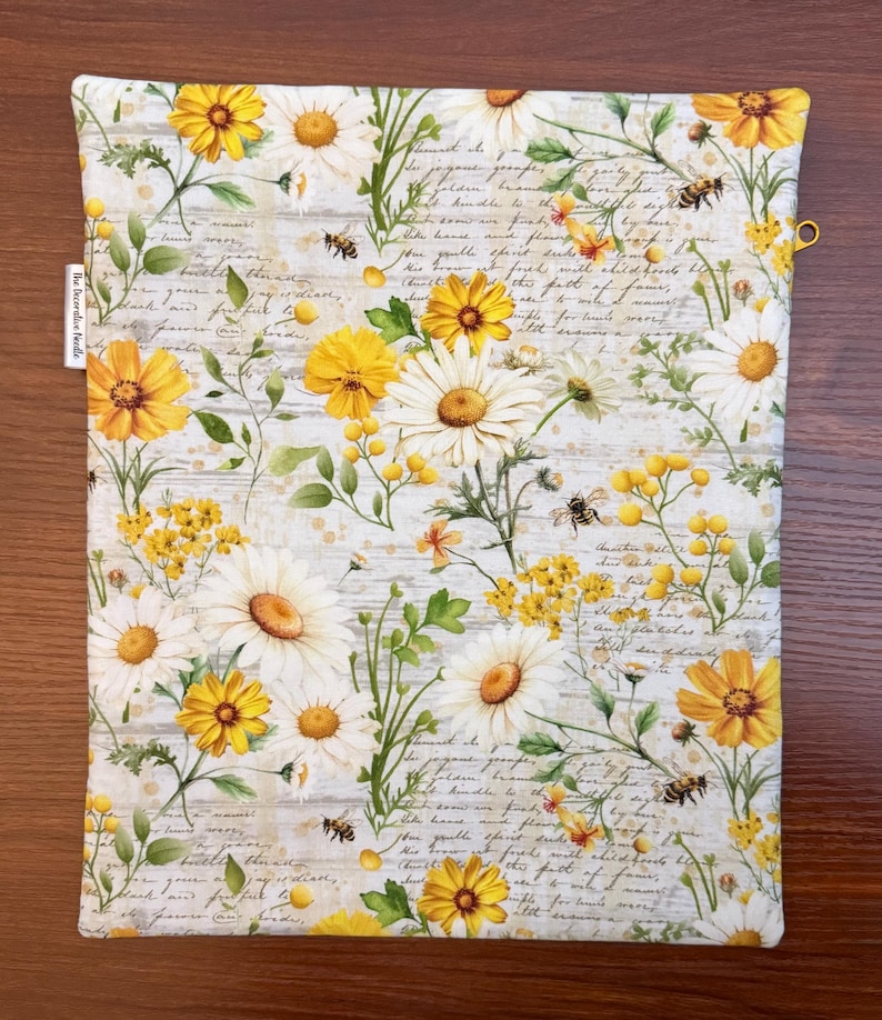 K&ouml;nnte beinhalten: Ein rechteckiger Stoffbeutel mit einem botanischen Druck aus wei&szlig;en und gelben G&auml;nsebl&uuml;mchen, gelben Wildblumen und kleinen Bienen vor einem Hintergrund aus blassem, kursivem Text. Ein kleines wei&szlig;es Stoffetikett mit der Aufschrift The Decoration Needle ist angebracht.