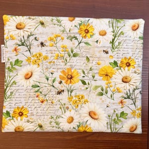 K&ouml;nnte beinhalten: Ein quadratischer Stoffartikel mit einem Muster aus wei&szlig;en G&auml;nsebl&uuml;mchen, gelben Wildblumen und kleinen Bienen auf einem Hintergrund aus hellgrauem Schreibschrifttext. Der Stoff hat ein kleines wei&szlig;es Etikett mit dem Text The Decoration Needle.