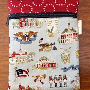 Op de afbeelding: Een rechthoekig etui met ritssluiting. De bovenkant is rood met witte sterren en de body is lichtblauw met patriottische illustraties. Deze omvatten een adelaar, gebouwen, vlaggen en soldaten. De rits is marineblauw.