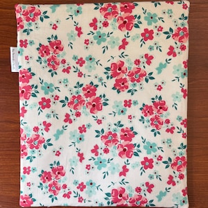Puede incluir: Un art&iacute;culo de tela rectangular con estampado floral. La tela presenta un fondo blanco con un patr&oacute;n repetido de flores rosas y turquesas y hojas verdes. El art&iacute;culo tiene una etiqueta que dice "The Decorative Handi".