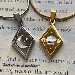 May include: Two silver and gold necklaces with pendants featuring a crescent moon and a planet with rings. The pendants are both diamond-shaped with a delicate, intricate design. The necklaces are on a white background with text that reads "love you" and "Le Petite Sprout".