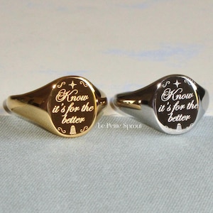 Puede incluir: Dos anillos de sello ovalados, uno dorado y otro plateado. Ambos anillos tienen una inscripción grabada que dice "Know it's for the better" y un pequeño gráfico de un fantasma.