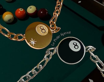 May include: Two gold and silver chain bracelets with a black and white 8 ball charm and a gold 8 ball charm with a small diamond accent. The bracelets are on a green felt pool table.