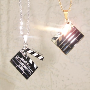 May include: Two silver and gold necklaces with a clapperboard pendant. The silver necklace has the text "For all those who found themselves in film." The gold necklace has a shiny, reflective surface.