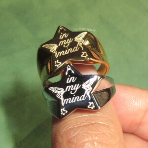 Pu&ograve; includere: Due anelli a forma di stella, uno in argento e uno in oro, con l'iscrizione "A in my mind" e "in my mind". Gli anelli sono indossati su un dito.