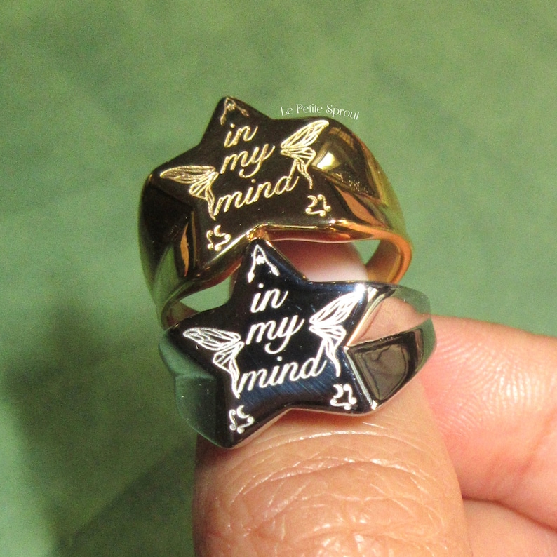 Pu&ograve; includere: Due anelli a forma di stella, uno in argento e uno in oro, con l'iscrizione "A in my mind" e "in my mind". Gli anelli sono indossati su un dito.