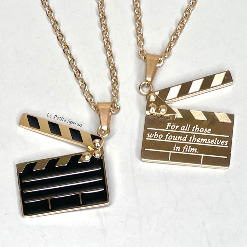 May include: Two gold necklaces with a clapperboard pendant. One pendant has black and white stripes and the other has the text "For all those who found themselves in film."