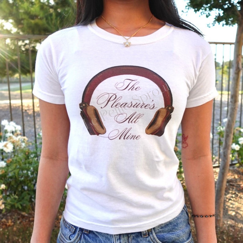 May include: White t-shirt with a graphic of headphones and the text "The Pleasure's All Mine" in a script font. The headphones are brown and burgundy. The shirt is a crew neck.