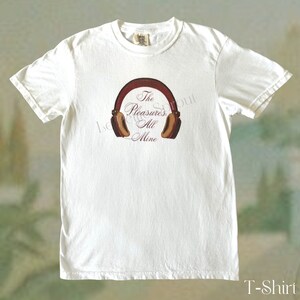 May include: White t-shirt featuring a brown and tan illustration of headphones with the text "The Pleasures All Mine" in a cursive font. The shirt is a classic crew neck style.