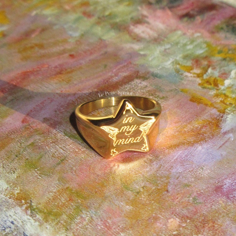 Pu&ograve; includere: Anello dorato con un design a forma di stella. La stella ha le parole "in my mind" incise.