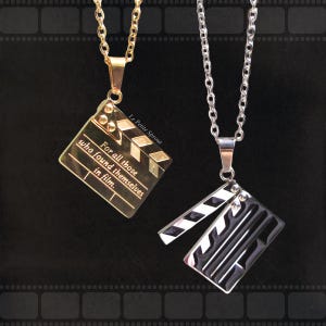 May include: Two silver chains with black and gold clapperboard pendants. The gold clapperboard pendant has the text "For all those who found themselves in film." and "Le Petite Sprout".