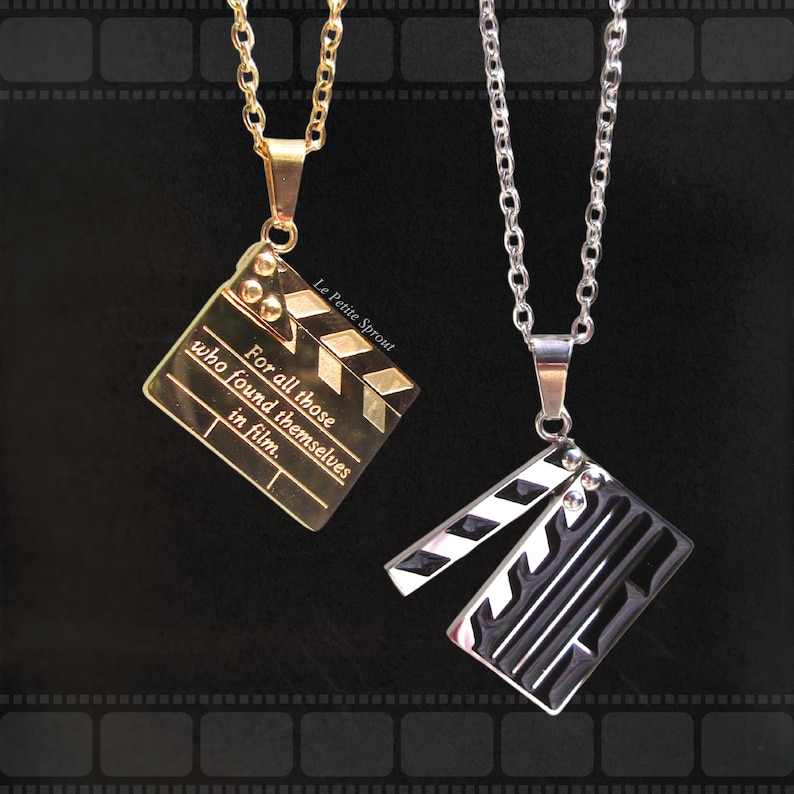 May include: Two silver chains with black and gold clapperboard pendants. The gold clapperboard pendant has the text "For all those who found themselves in film." and "Le Petite Sprout".