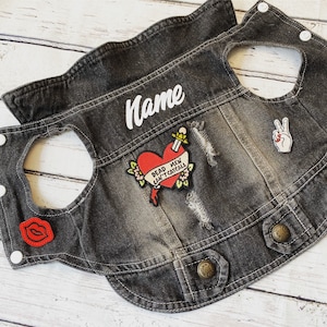 May include: A black denim jacket with patches, including a red heart with a dagger and the text "Dead Men Can't Catcall", a peace sign, and a red lip. The jacket has a white embroidered name tag that says "Name".