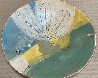 May include: Hand-painted ceramic bowl with a floral design. The bowl features a white, blue, yellow, and green color palette. The floral design is outlined in black. The rim of the bowl is red.