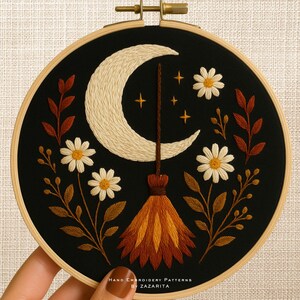 May include: Embroidered artwork in a wooden hoop featuring a crescent moon, stars, daisies, and a broom against a black background. The text "Hand Embroidery Patterns By Zazarita" is at the bottom.