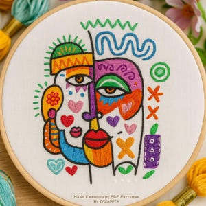May include: A colorful hand-embroidered artwork in a wooden hoop. The design features a stylized face with vibrant colors, including orange, purple, blue, and green. Hearts and geometric shapes add to the abstract design. The text "Hand Embroidery PDF Patterns By Zazarita" is at the bottom.