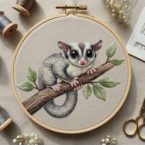 Puede incluir: Bordado artesanal de una zarigüeya del azúcar posada en una rama con hojas verdes. La zarigüeya del azúcar tiene pelaje gris y blanco, ojos grandes y negros y patas rosas. El bordado está en un bastidor de madera.