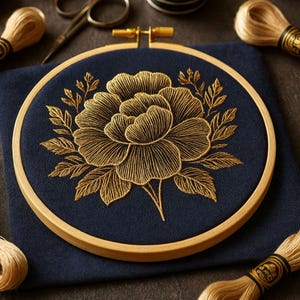 Könnte beinhalten: Ein goldfarbenes Blumenmuster auf marineblauem Stoff, gestickt in einem Holzrahmen. Das Design zeigt eine große Blüte und Blätter. Garnrollen und eine Schere sind ebenfalls im Bild zu sehen.