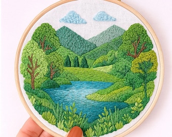 May include: A hand-stitched embroidery piece showing a tranquil landscape. The design includes a blue lake, green trees, and hills under a light blue sky with two clouds. The embroidery is set in a 15 cm wooden hoop, displaying a detailed nature scene.