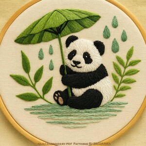 Peut inclure: Broderie d'un panda noir et blanc tenant un parapluie vert sous la pluie. Des gouttes vertes et des feuilles sont brodées sur un fond beige. Le tout est encadré dans un cercle en bois.