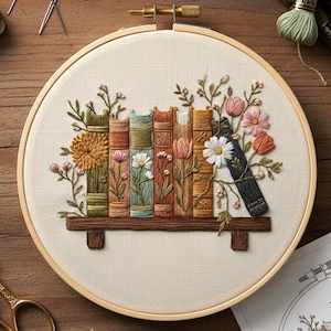 May include: Embroidered hoop art featuring a bookshelf with colorful books and floral accents. The books are in shades of green, orange, and brown, with pink and white flowers. The embroidery is set in a wooden hoop.