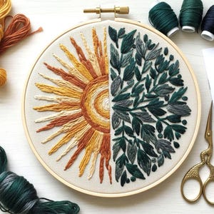 Peut inclure: Un cercle à broder avec un motif divisé : un soleil aux couleurs jaune et orange d'un côté, et un motif de feuilles vertes de l'autre. L'œuvre est réalisée sur un fond de tissu neutre, avec un cercle en bois et des éléments dorés.