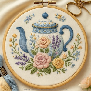 以下が含まれることがあります： 木製のフレームに入った、刺繍された花のティーポットのデザイン。 ティーポットは白と青で、ピンクと黄色のバラ、ラベンダー、緑の葉が描かれています。 下部には「Hand Embroidery PDF Patterns By Zazarita」の文字があります。
