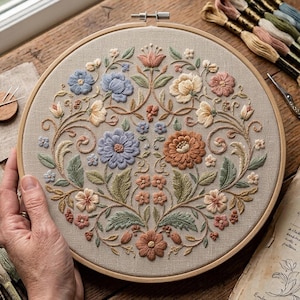 May include: A circular wooden embroidery hoop containing a beige fabric panel with a detailed floral design. The embroidery features symmetrical arrangements of flowers and leaves in shades of dusty pink, sage green, soft blue, and cream.