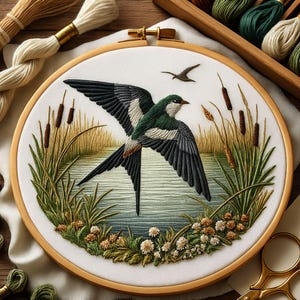 Op de afbeelding: Geborduurde borduurringkunst met een vogel in vlucht boven een meer. De vogel heeft groene, zwarte en witte veren. Het kunstwerk bevat riet, gras en kleine witte bloemen. De ring is van hout en de achtergrond is witte stof.