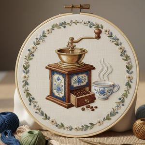Puede incluir: Arte de aro bordado con un molinillo de café, una taza de café y granos de café. El molinillo es marrón y dorado, con detalles florales azules. Un borde floral rodea la imagen central. La taza tiene un diseño floral azul.
