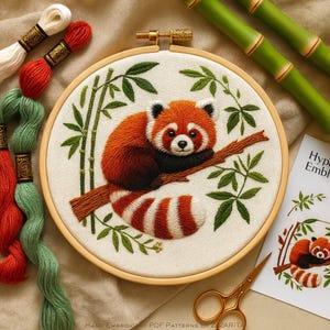 May include: An embroidered hoop art piece featuring a red panda perched on a branch, surrounded by bamboo and greenery. The red panda has a fluffy orange and white coat. Embroidery floss and bamboo stalks are visible.