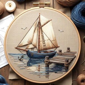 Op de afbeelding: Geborduurde nautische scène in een houten hoepel. Een blauw zeilbootje met witte zeilen is afgebeeld in de buurt van een houten pier. Het water weerspiegelt de boot en de pier. Twee zeemeeuwen vliegen boven het water. Borduurgaren en een patroon op de achtergrond.