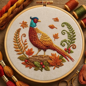 Puede incluir: Un faisán bordado en un aro de madera. El ave está representada en tonos naranja, amarillo y marrón, con la cabeza azul y roja. Hojas de otoño y vegetación rodean al faisán. Hilos de bordar y tijeras visibles.