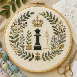 May include: Embroidered chess-themed hoop art. A black and white chess king and queen are centered, surrounded by a floral wreath with a gold crown at the top. The embroidery is on a cream-colored fabric, set in a wooden hoop.