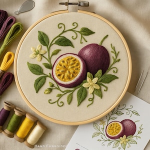 May include: Hand-embroidered passion fruit design on a beige fabric stretched in a wooden hoop. The embroidery features a whole passion fruit and a half, with green leaves and yellow flowers. Spools of thread in various colors are visible.
