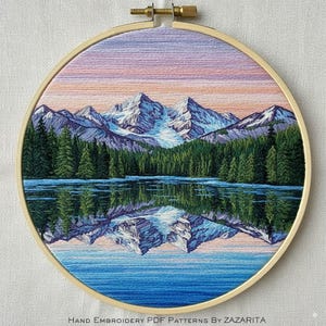 Peut inclure: Broderie à la main dans un cercle en bois représentant un paysage de lac de montagne. Des sommets enneigés se reflètent dans l'eau, encadrés par une forêt d'arbres verts. Le ciel passe du rose à l'orange, créant un paysage paisible. Le texte "HAND EMBROIDERY PDF PATTERNS BY ZAZARITA" est en bas.
