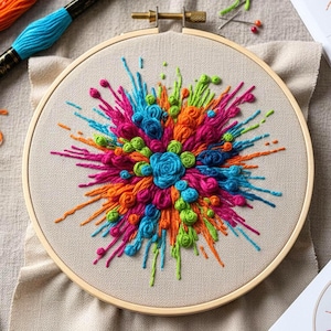 May include: A colorful embroidery hoop featuring a vibrant explosion of thread art. The design includes pink, orange, blue, and green threads, creating a dynamic and textured artwork. The embroidery is set in a wooden hoop.