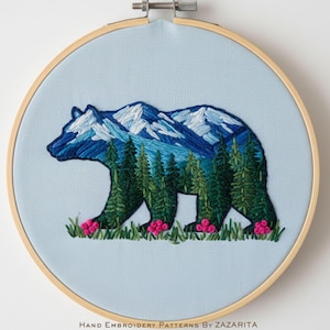 May include: Embroidered artwork of a bear silhouette filled with a mountain and forest scene. The bear is blue, the mountains are blue and white, and the trees are green. Pink flowers and green grass are at the bottom. The text "Hand Embroidery Patterns By Zazarita" is at the bottom.
