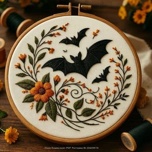 May include: Embroidered Halloween hoop art featuring three black bats, orange flowers, and green leaves. The design is set against a cream-colored fabric within a wooden hoop. Text at the bottom reads "Hand Embroidery PDF Patterns by Zazarita."