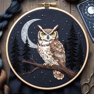 May include: An embroidered owl perched on a branch, set against a dark blue night sky with a crescent moon and pine trees. The owl has brown and white feathers, with yellow eyes. The embroidery is framed in a wooden hoop.