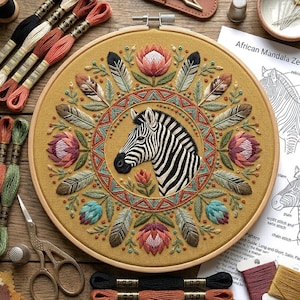 May include: A circular embroidery hoop containing a mustard yellow fabric with a hand-stitched zebra head at the center. The design features a geometric border, surrounding protea flowers, and feathers in shades of pink, green, and brown.