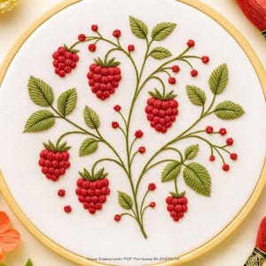 May include: Hand-embroidered raspberry design on white fabric stretched within a wooden hoop. The artwork features detailed red raspberries, green leaves, and small red berries on green stems. The text "Hand Embroidery PDF Patterns by Zazarita" is at the bottom.
