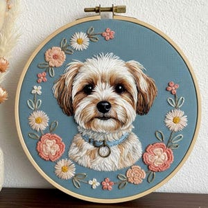 May include: Embroidered portrait of a dog in a wooden hoop. The dog has brown and white fur, a blue collar, and is surrounded by embroidered flowers in shades of pink, peach, and white against a blue background.